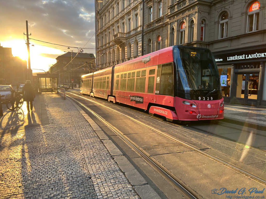 A modern tram moving towards the camera with the sun setting behind it
