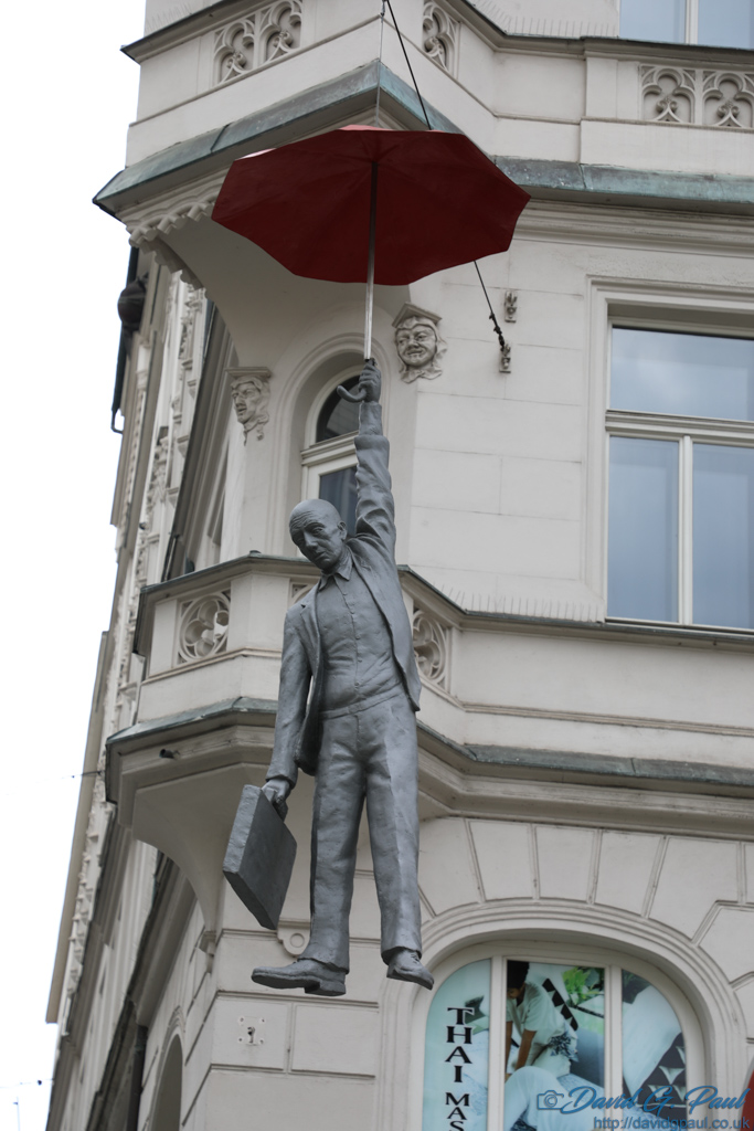 A staue suspended above a street, looking like it's falling from an umbrella