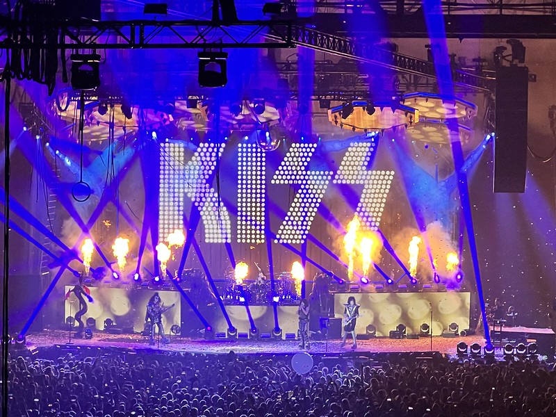 Kiss performing on stage with flames behind them and the logo in lights
